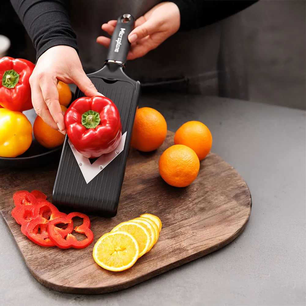 Person bruger Microplane Mandolin V-slicer til at lave skiver af rød peberfrugt