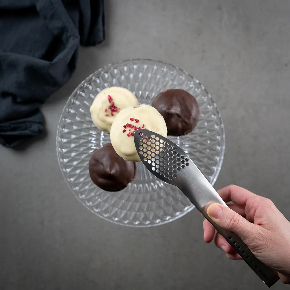 Person løfter et stykke konfekt med hvid chokolade med Global serveringstang GS-65 på 23 cm
